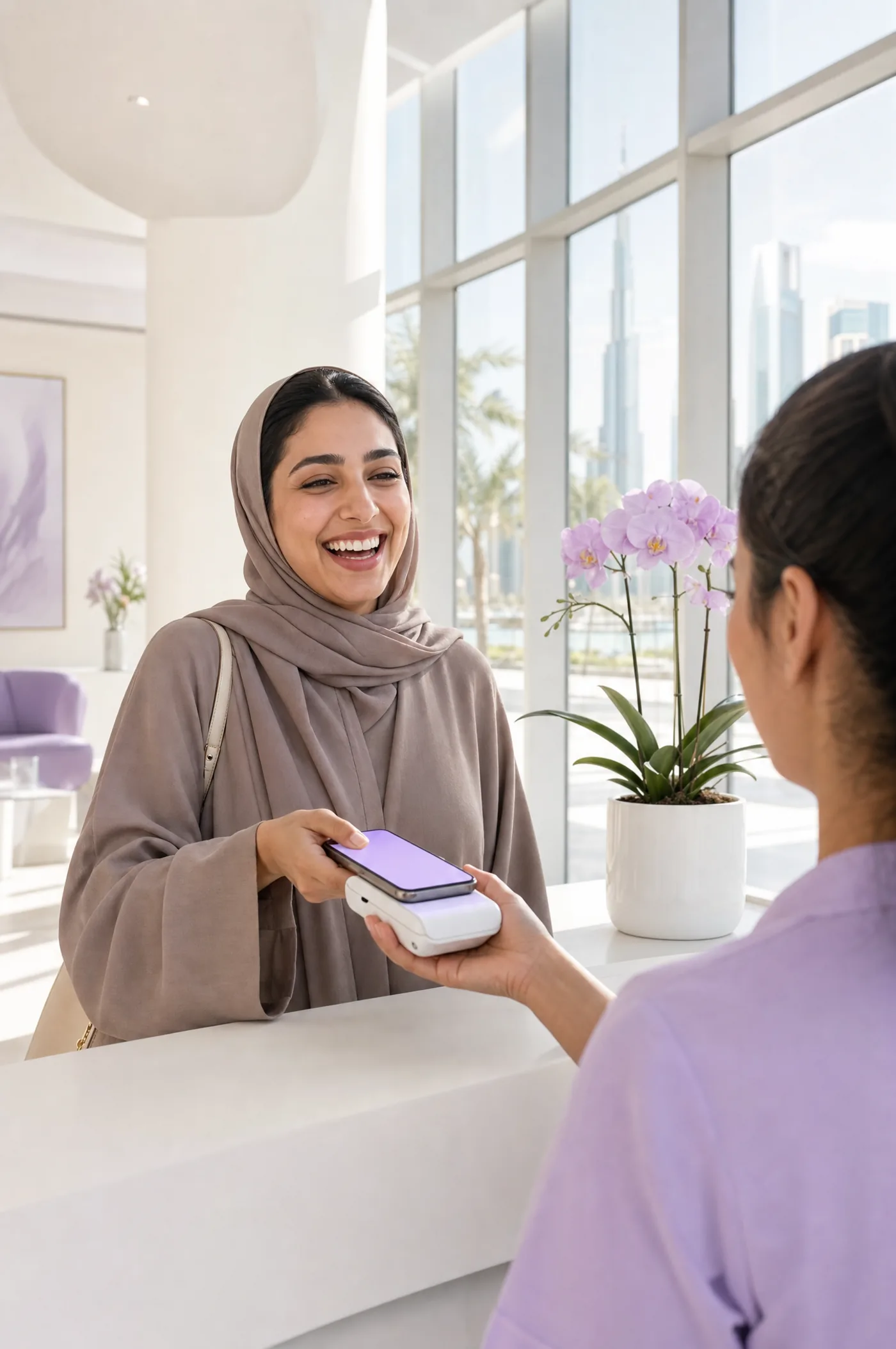 عميلة تدفع بهاتفها عند مكتب استقبال عيادة مضيئة، ويظهر خلفها أفق دبي